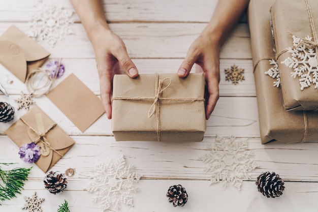 Chiuda in su del contenitore di regalo del presente della donna delle mani sulla tabella di legno con la decorazione di natale.