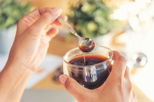 Chiuda sulle mani della donna seduta alla scrivania dell'ufficio con una tazza di caffè dolce rilassarsi e divertirsi con il tempo felice tazza di caffè caldo in mano donna che tiene una tazza di caffè rilassante dopo il lavoro in ufficio gusto caldo nella caffetteria