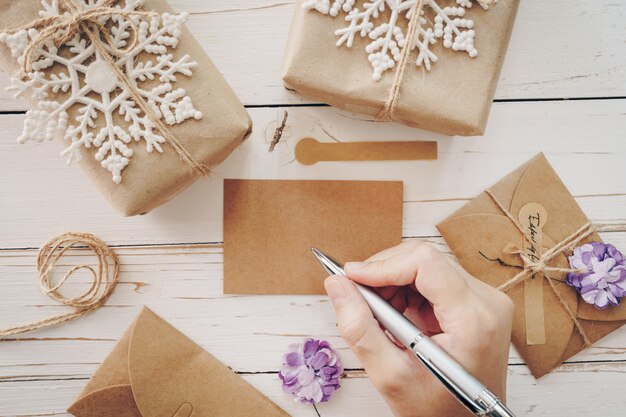 Foto chiuda su della donna delle mani che scrive la lista dei desideri e la cartolina di natale vuote sulla tavola di legno con la decorazione di natale.