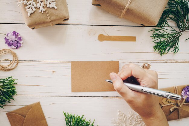 Foto chiuda su della donna delle mani che scrive la lista dei desideri e la cartolina di natale vuote sulla tavola di legno con la decorazione di natale.