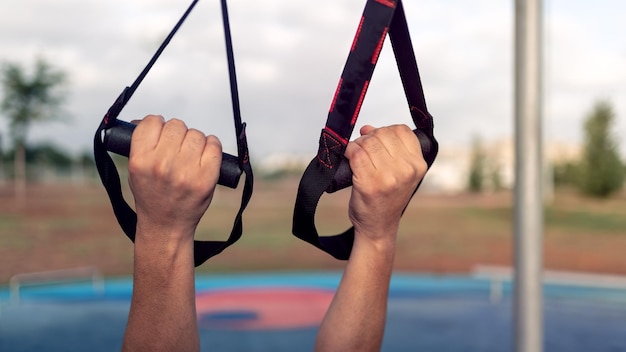 Close up hands of young man doing fitness exercises on a special hanging device