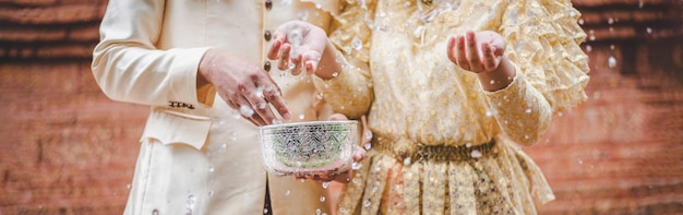 Close up hands of Young man and woman dressed in beautiful Thai costumes splashing in Temple and preserve the good culture of Thai people during Songkran festival Thai New Year Family Day in April