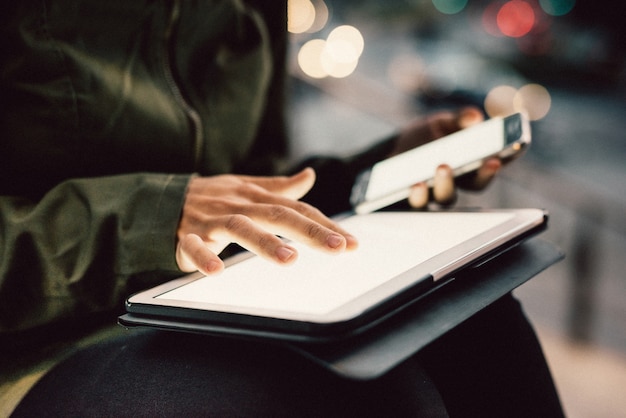 Close up on the hands of young woman using smartphone and tablet in the city night