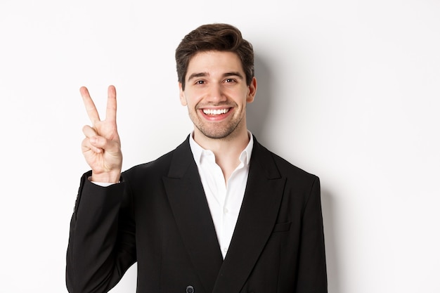 Close-up of handsome businessman in black suit, smiling amazed, showing number two, standing over