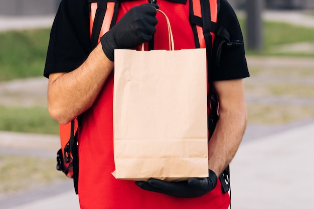 Close up handsome courier man holding paper bag with food at street outdoors worker grocery to house