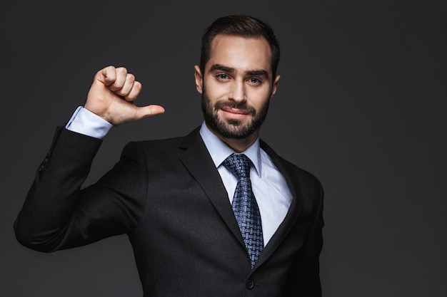 Close up of a handsome young business man wearing suit standing isolated, pointing at himself