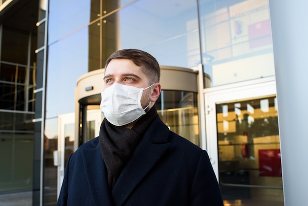 Крупным планом красивый молодой человек кавказской, выходя из своего офиса, носить хирургический маска