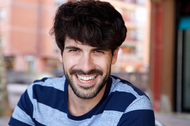 Close up handsome young man with beard laughing outside