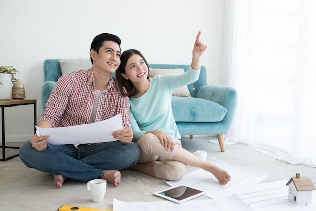 Close up of happy asian couple looking at blueprint at home