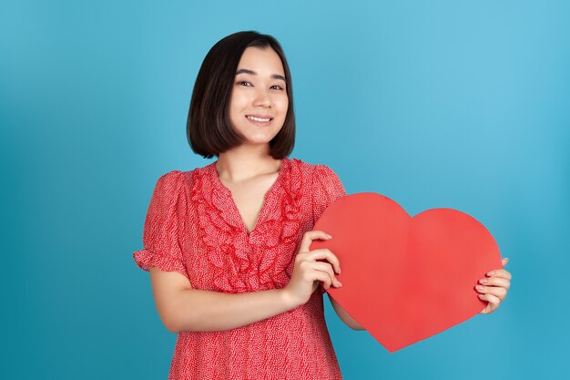 Close-up happy beautiful young asian woman in red dress holding big red paper heart