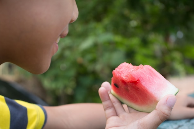 幸せな少年のクローズアップは、緑の自然の背景にスイカを保持しています。