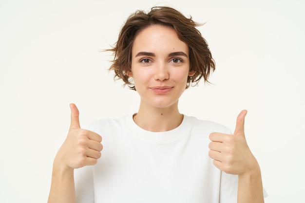 Photo close up of happy brunette woman shows thumbs up approves something recommends gives positive