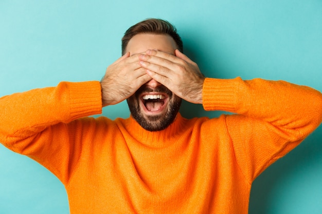 Close-up of happy caucasian man waiting for surprise, close eyes and smiling, standing