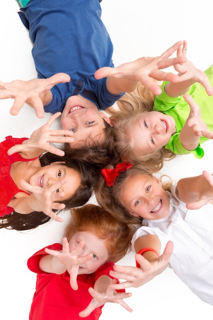 Close-up of happy children lying on floor in studio and looking up, isolated on white background, top view. Kids emotions and fashion concept