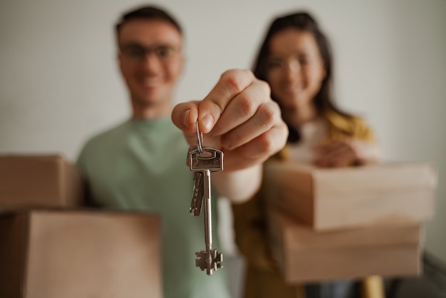 Фото Закройте вверх по счастливой паре, держащей ключи от новой квартиры с коробками. молодая семья переезжает в новую квартиру.