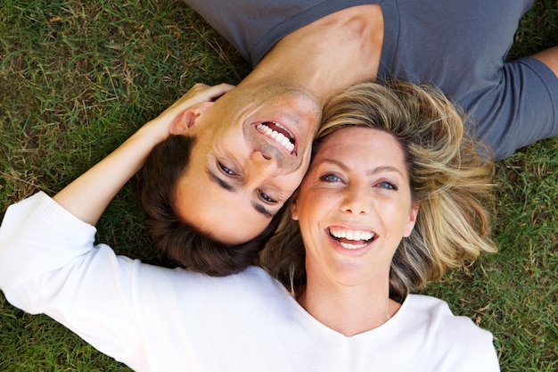 Close up happy couple lying on grass together laughing