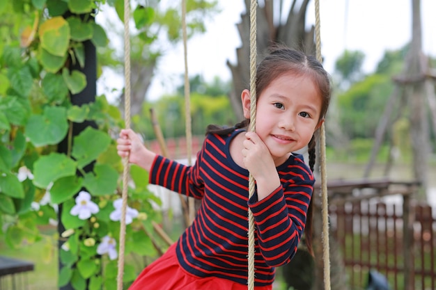 Close up happy little Asian child girl play and sitting on the swing in the nature park.