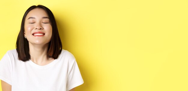 Close up of happy and relaxed asian woman enjoying sun smiling with eyes closed and looking joyful s