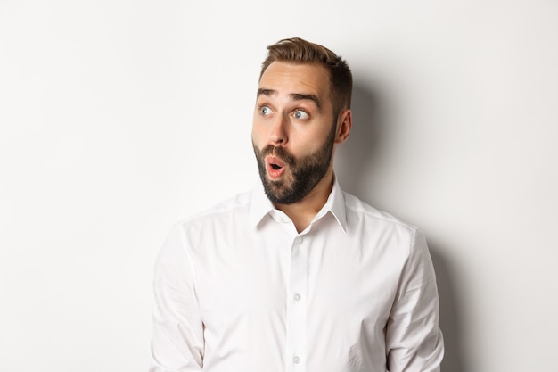 Close-up of happy and surprised man looking left with amazed face, white background.