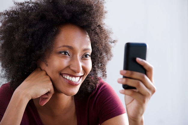 Chiuda sulla giovane donna africana felice che per mezzo dello smart phone