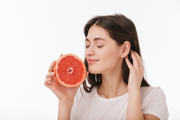 Close up of a happy young beautiful woman isolated, showing fresh sliced grapefruit