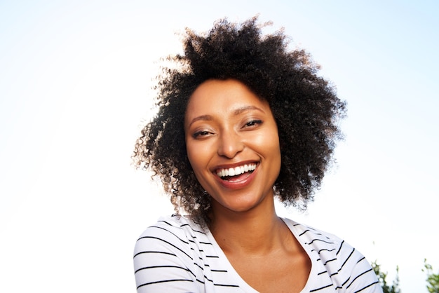 Close up happy young black woman laughing outdoors against bright sunshine
