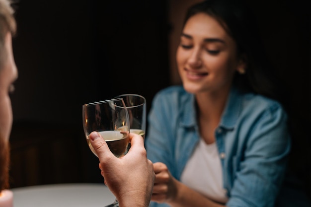 Close-up of happy young couple clinking glasses with wine sitting at table with candles in cozy dark room. Loving man and woman celebrating anniversary, Valentines day, enjoying romantic date.