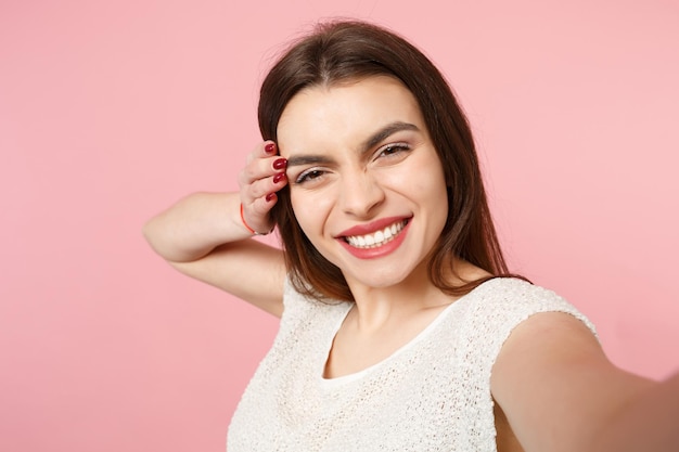 Primo piano di giovane donna felice in abiti leggeri casual in posa isolata su sfondo rosa pastello parete ritratto in studio. concetto di stile di vita delle persone. mock up spazio di copia. facendo selfie sul cellulare.