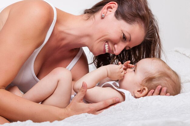 Photo close-up of happy young woman lying with baby on bed