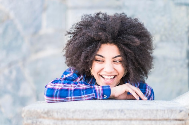 Close-up of happy young woman with curly hair on retaining wall