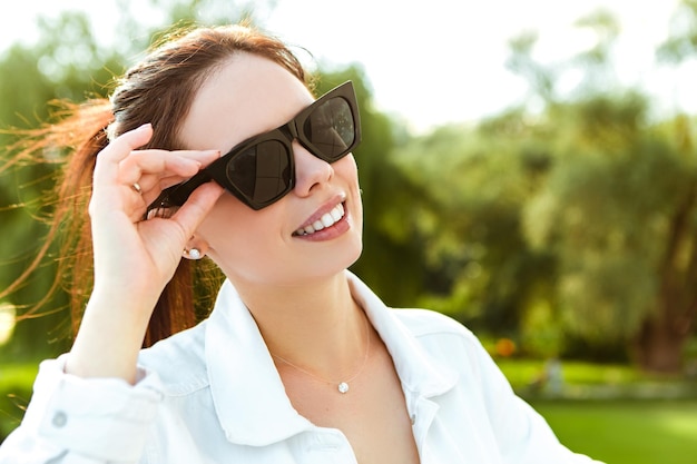 Close up head portrait of smiling caucasian woman with white teeth hold sunglasses