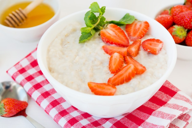 Close up healthy balanced Breakfast of oatmeal with strawberries and honey on a white wall. Horizontal photo.