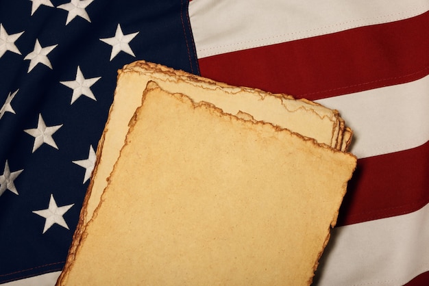 Photo close up heap of blank vintage yellow paper sheets on old weathered cotton embroidered us national flag, symbol of american history, elevated high angle view, directly above