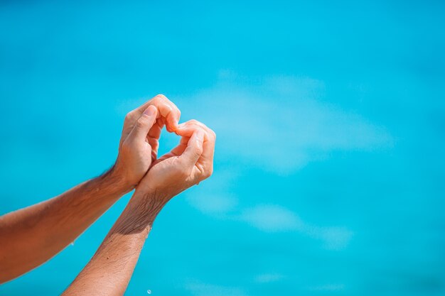 Close up of heart made by female hands background the turquoise ocean