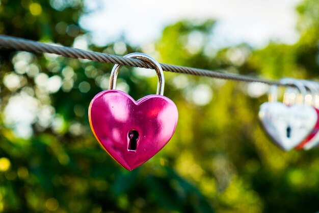 Photo close-up of heart shape padlocks hanging on cable