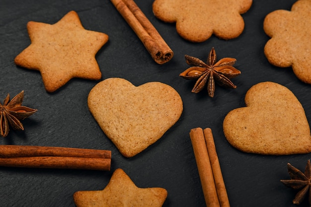 Photo close up heart and star shaped christmas gingerbread cookies with cinnamon and star anise spices on black slate background, elevated top view, directly above