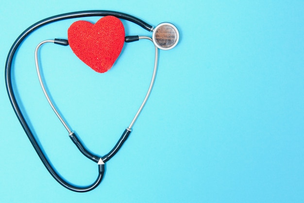 Foto primo piano di un cuore e uno stetoscopio su sfondo blu, vista dall'alto. concetto globale di assistenza sanitaria. prendersi cura della salute del cuore. trattamento con compresse e fiale