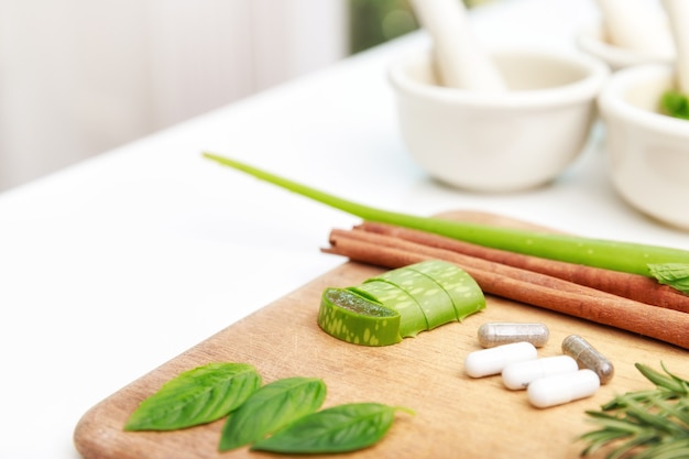 Close up of Herbal medicine preparation with fresh herbs and dried flowers, aromatherapy essential oil and mortar with pestle used in natural alternative remedies on white table.