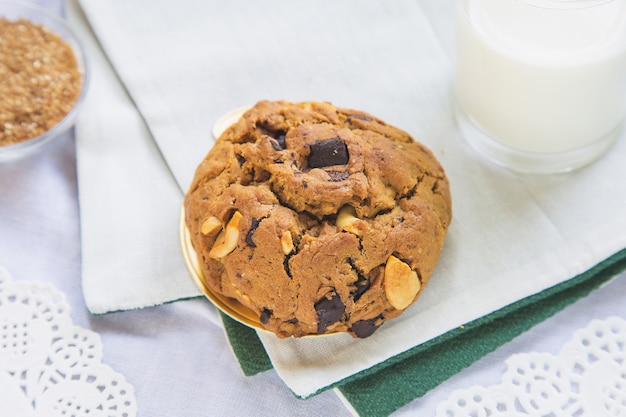 ブラウンシュガーの背景に牛乳のカップと白いテーブルの上の高角度ビューチョコレートチップクッキーを閉じる