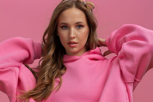 close-up horizontaal portret van een jonge vrouw in een roze oversized hoodie op een roze achtergrond