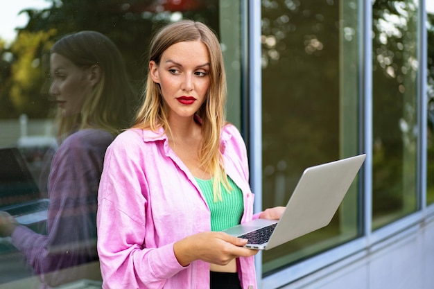 Close up horizontal picture of blonde stylish woman using her laptop, bright make up positive mood, work and study.