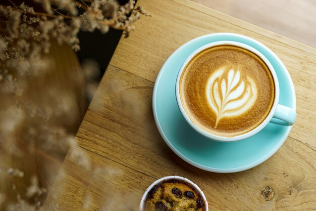 Close-up of Hot coffee latte with latte art milk foam in cup mug and Homemade Banana cup cake on wood desk office desk in coffee shop at the cafe,during business work concept