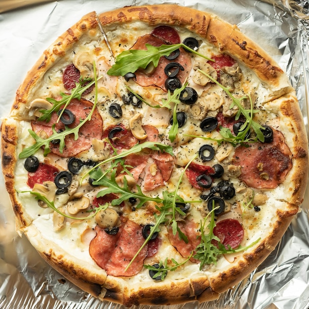 Close-up of hot pizza with olives, salami and mozzarella on foil. Copy space.