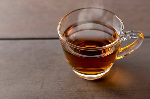 Закройте чашку горячего чая на деревянном столе. горячий чай в ручке стакана.