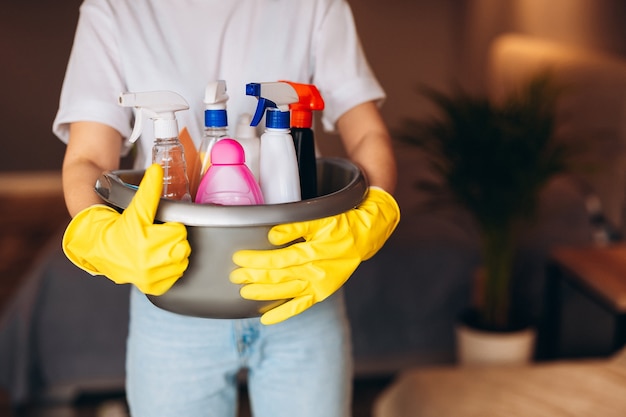 close up housekeeper in yellow glove is holding toe full of detergents at home