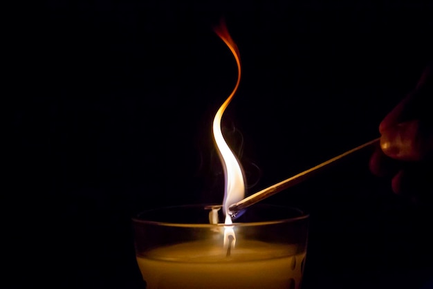 Foto close-up di mano umana che brucia una candela con un fiammifero su uno sfondo nero
