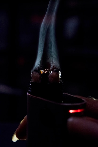 Photo close-up of human hand holding burning electronic cigarette at night