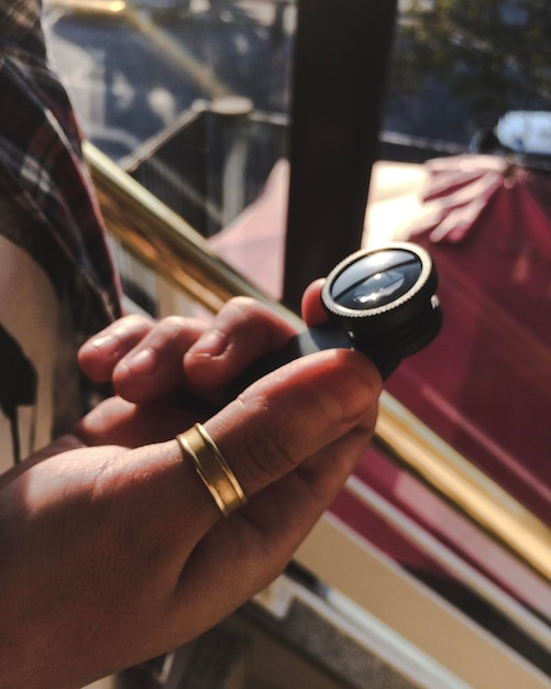 Photo close-up of human hand holding camera lens by window