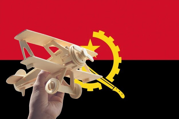 Foto close-up di un modello di aereo tenuto dalla mano umana contro la bandiera dell'angola