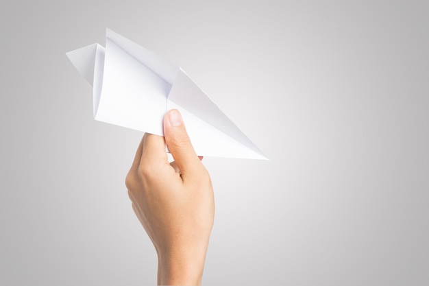 Foto close-up di una mano umana che tiene un aereo di carta su uno sfondo grigio